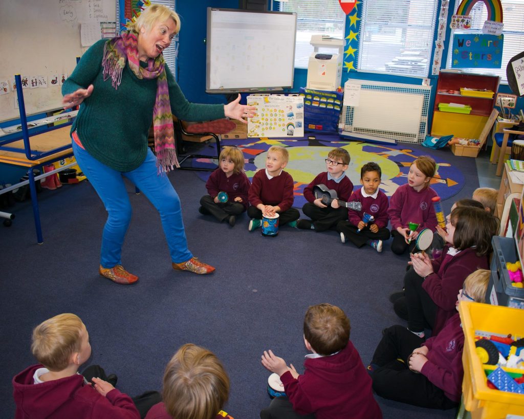 Lilian Ross is singing a song with actions to young pupils.