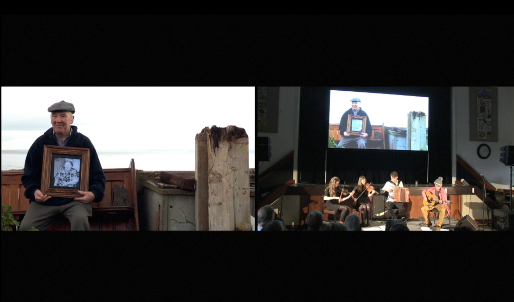 Video still from Kin in the Community featureing older man holding an old-fashioned portrait of a woman, alongside young musicians playing on a stage