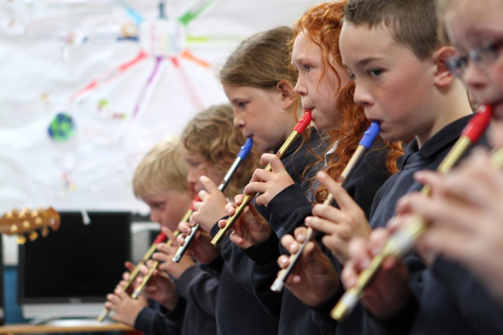 Young tin whistle players stand in line and play a tune together.